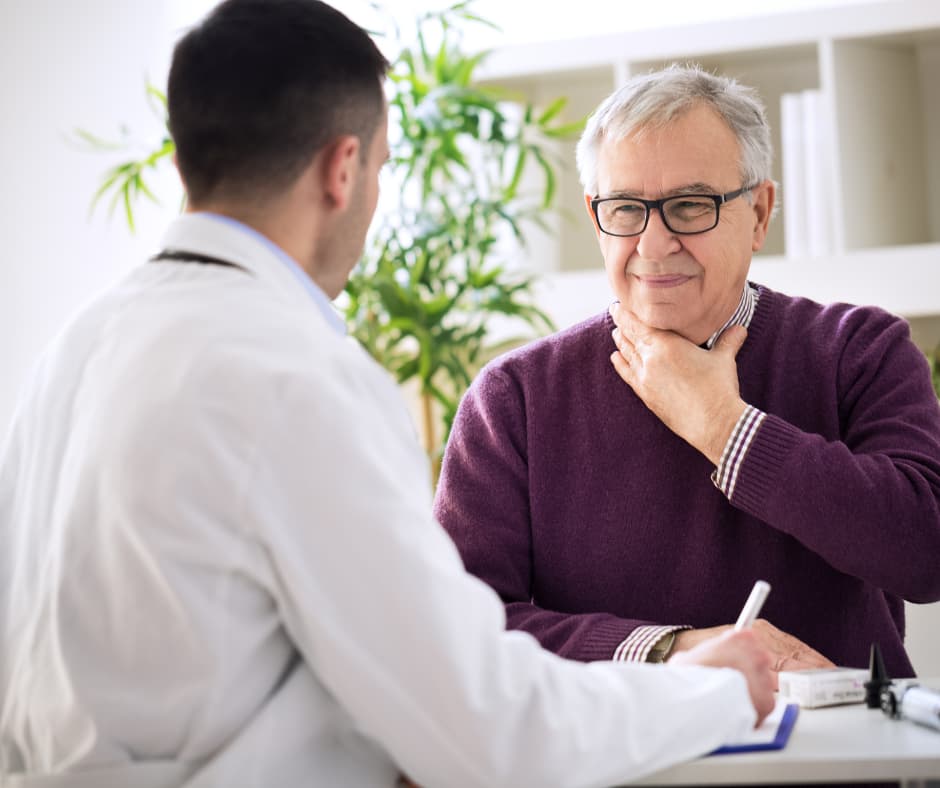Man speaks to doctor while holding his throat.